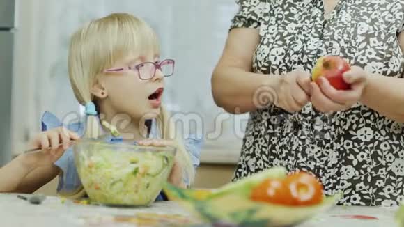 去看望奶奶一个6岁的女孩吃沙拉旁边的一个老妇人正在用刀子给她清洗一个苹果视频的预览图