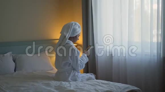 穿白色浴袍的年轻女子坐在酒店的床上视频的预览图