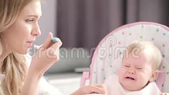 妈妈用勺子喂宝宝小孩在婴儿椅上哭视频的预览图