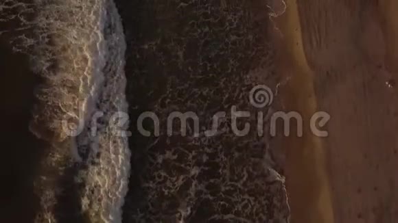 飞在海水之上的无人机白色的泡沫溅在沙质的海岸上傍晚海滩上的鸟瞰海浪视频的预览图