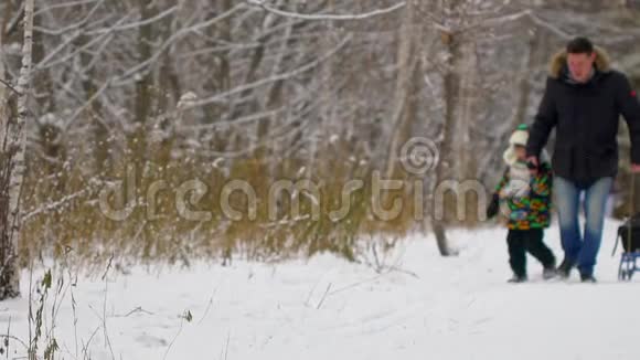快乐的父亲和一个非常可爱快乐的小男孩他的儿子在一个雪冬公园里跑步微笑的男孩有魅力的家庭视频的预览图