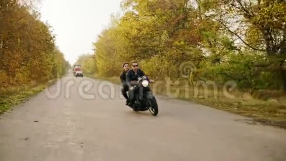 追踪一对夫妇在森林道路上骑摩托车在秋天戴墨镜的漂亮小伙子开车视频的预览图