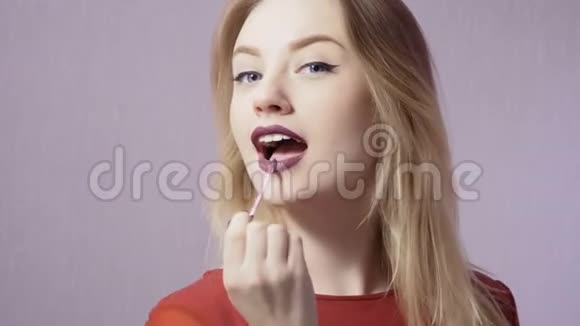 可爱的金发女郎用紫色的唇彩涂着她的嘴唇视频的预览图
