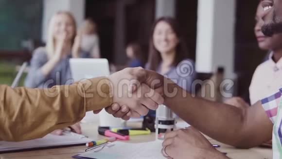 两个伙伴非洲和高加索商人握手一群人在办公室的背景上鼓掌慢节奏视频的预览图