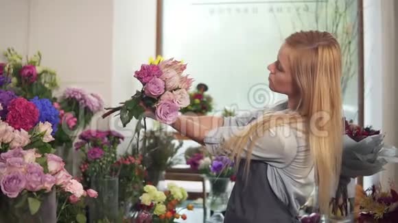 一位穿着围裙的年轻漂亮女人在花店工作布置一束花她看上去很漂亮视频的预览图