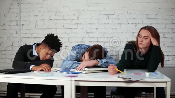 年轻的学生在讲课时感到无聊而其中一个正坐在桌边睡觉视频的预览图