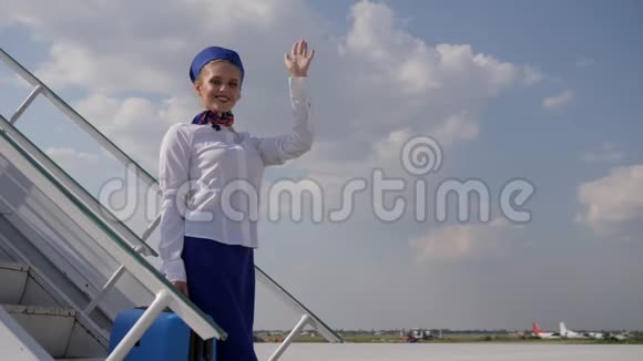 机场女工作人员在机场的楼梯上挥手拿着手提箱视频的预览图
