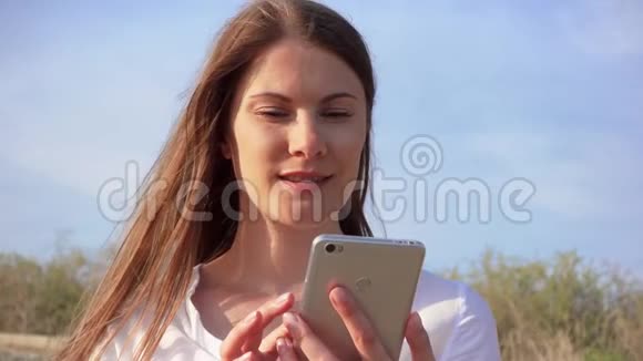女人用手机对抗蓝天微笑女性通过手机慢动作与朋友聊天视频的预览图