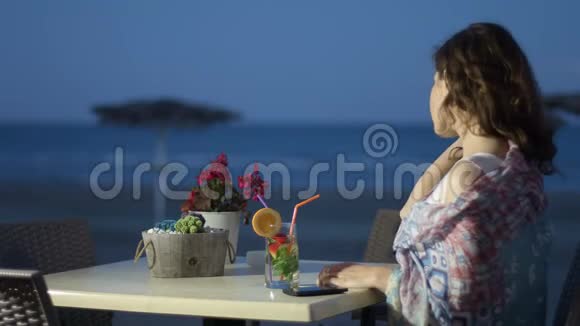 浪漫的年轻女人喝鸡尾酒梦幻的女人看着夜晚的海景视频的预览图