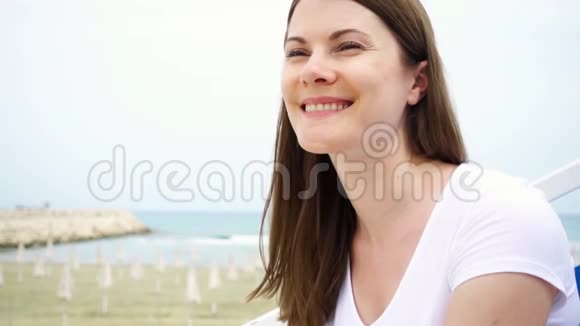 动作缓慢坐在海滩上的年轻女人的肖像从地中海吹来的风吹过她的头发视频的预览图