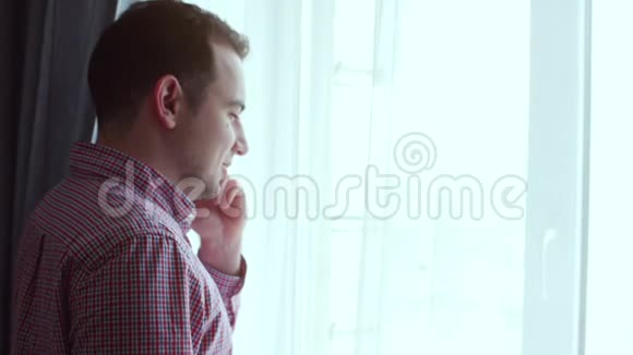 穿格子衬衫的年轻人一边看着窗外一边用红色电话说话视频的预览图
