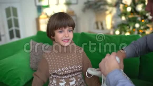 这位年轻的父亲给他的小儿子戴上了一顶温暖的帽子坐在家里的沙发上背景是圣诞树慢慢慢慢视频的预览图