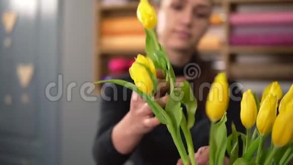年轻迷人的微笑女人穿着围裙在花店工作用新鲜的黄色郁金香插花视频的预览图