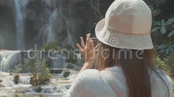 一位年轻女子站在瀑布旁用智能手机拍照视频的预览图