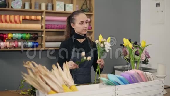 年轻的女花匠站在桌旁的花店里摆弄现代花束她把奶油玫瑰和视频的预览图