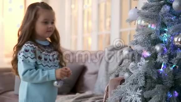 穿蓝色毛衣的小女孩被圣诞树球装饰着视频的预览图