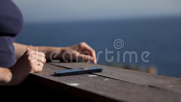 一位年轻迷人的女士在温泉酒店的阳台上使用智能手机一位女士正在海边拍摄日落视频的预览图