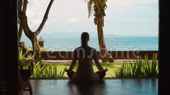 在巴厘岛海边的平房里在莲花的位置练习瑜伽让女人的剪影放松美丽的景色视频的预览图