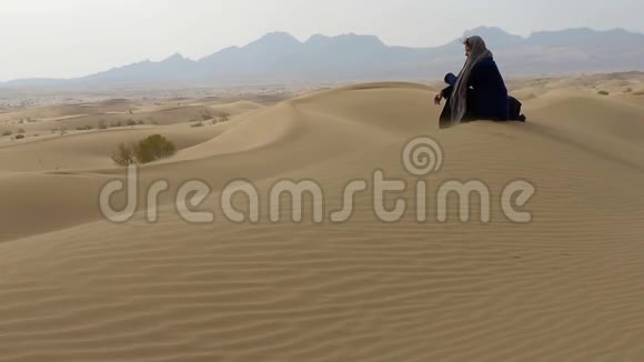 一个孤独的女孩坐在沙漠中的沙丘上视频的预览图