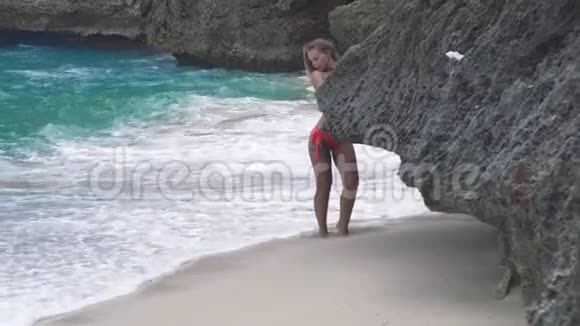 性感的女人在岩石海滩和海浪背景上摆姿势穿着泳装的迷人女人在夏天的海滩上休息视频的预览图