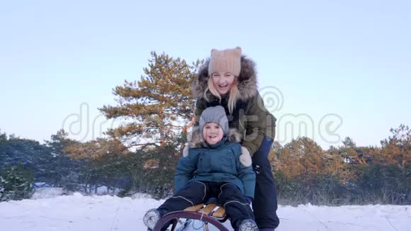 冬天母亲推着儿子上雪橇他慢悠悠地从雪山上骑马视频的预览图