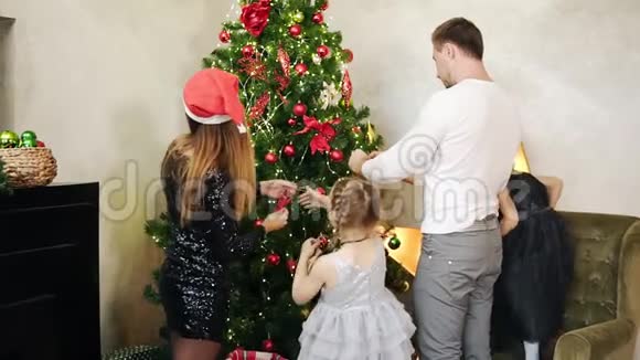 一位母亲戴着圣诞老人的帽子父亲和两个可爱的女儿装饰着年轻快乐的家庭视频的预览图