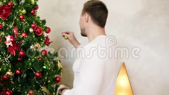 年轻人拿着一个球挂在一棵人造圣诞树上的背面在家装饰圣诞树慢动作视频的预览图