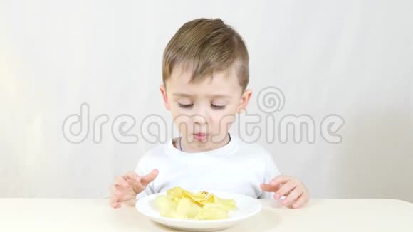 一个孩子正在吃盘子里的薯片坐在白色背景的桌子旁视频的预览图
