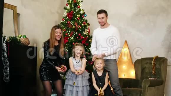 年轻幸福的四口之家站在圣诞树旁扔出金色的纸屑可爱的母亲父亲和两个视频的预览图