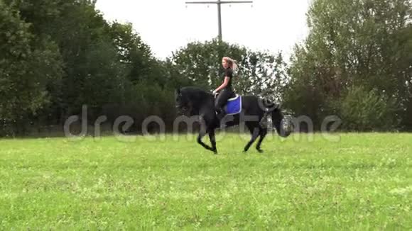 美丽的金发女郎骑着一匹黑马骑着田野视频的预览图