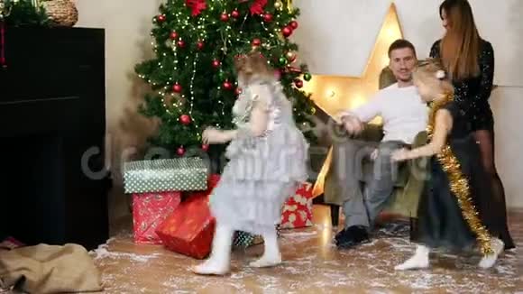 小女孩在房间里跑来跑去从圣诞树下拿出礼物送给他们的父母和视频的预览图