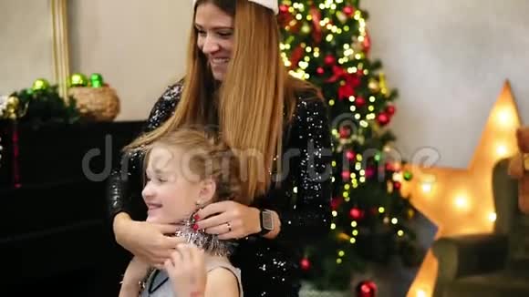 年轻快乐的母亲戴着圣诞老人的帽子帮女儿装饰自己的圣诞礼物放银视频的预览图