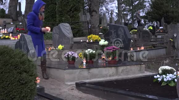 悲伤的女人坐在墓地的坟墓上手里拿着燃烧的蜡烛祈祷4K视频的预览图