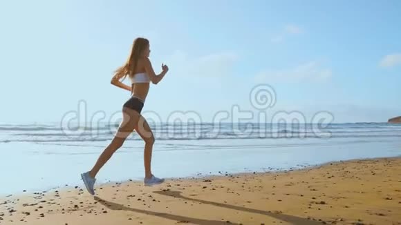 一位身材苗条的年轻女子在日出时在海上从事体操她沿着海岸跑步视频的预览图