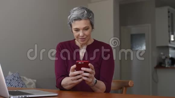 快乐的成熟女人在家里使用智能手机视频的预览图