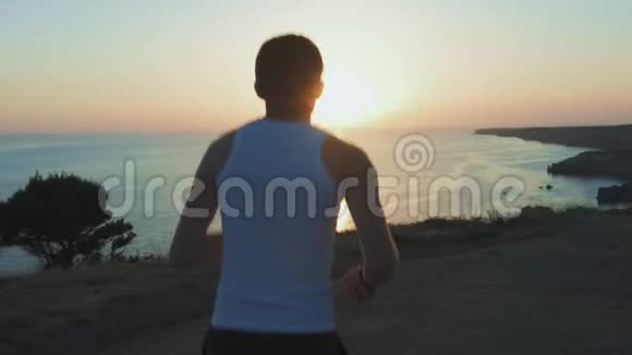运动帅哥正在用手机和耳机做运动在日落时沿着海岸跑步然后慢跑视频的预览图