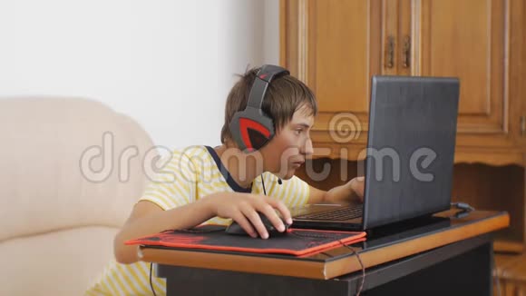使用笔记本电脑的青少年带着耳机的青少年男孩用电脑游戏鼠标粘在笔记本屏幕上视频的预览图