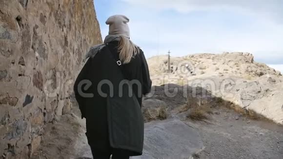 一位身穿绿色皮夹克的年轻女游客走在一座古老修道院的堡垒墙边视频的预览图
