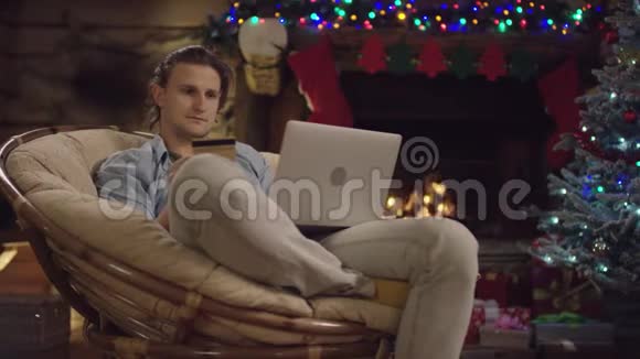 圣诞夜用笔记本电脑和信用卡在线购物的帅哥视频的预览图