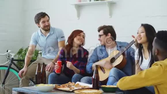 快乐的年轻朋友在共享公寓聚会一起唱歌而他们的朋友在家弹吉他视频的预览图