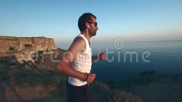 运动帅哥正在用手机和耳机做运动在日落时沿着海岸跑步然后慢跑视频的预览图