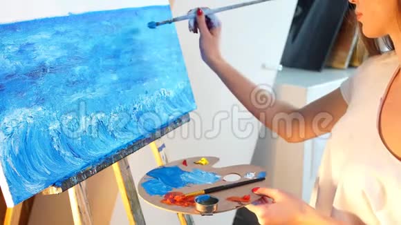 一位年轻的女艺术家在她的车间里用蓝色油画颜料在画布上作画视频的预览图