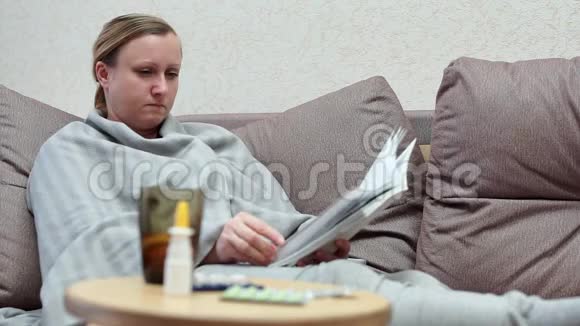 一个女人家里感冒了躺在沙发上用一本书上面盖着一条毯子视频的预览图