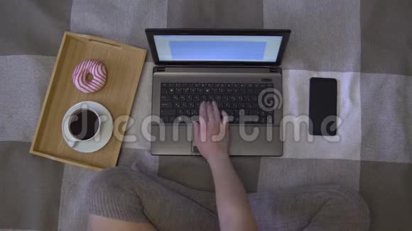一个女孩用笔记本电脑在家里坐在床上喝咖啡4K视频的预览图