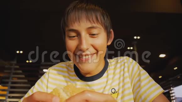 青少年吃快餐在快餐店里一个饥饿的少年咬芝士汉堡的特写镜头视频的预览图
