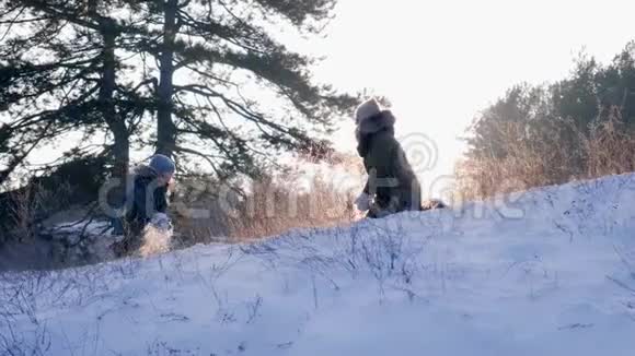 男孩和妈妈在美丽的冬天和户外日落的背景下玩雪视频的预览图