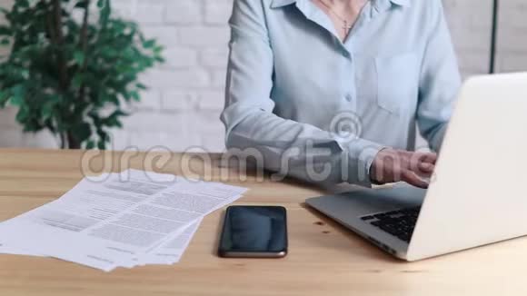 妇女在办公室的办公桌上使用笔记本电脑和智能手机视频的预览图