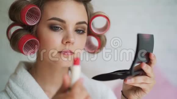 洗澡后的早晨一个穿着卷发衣的漂亮女孩在画她的嘴唇视频的预览图