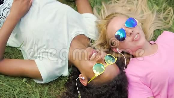 两个美丽的女孩躺在草地上一起听音乐和唱歌视频的预览图