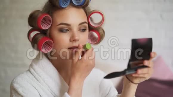 洗澡后的早晨一个穿着卷发衣的漂亮女孩在画她的嘴唇视频的预览图